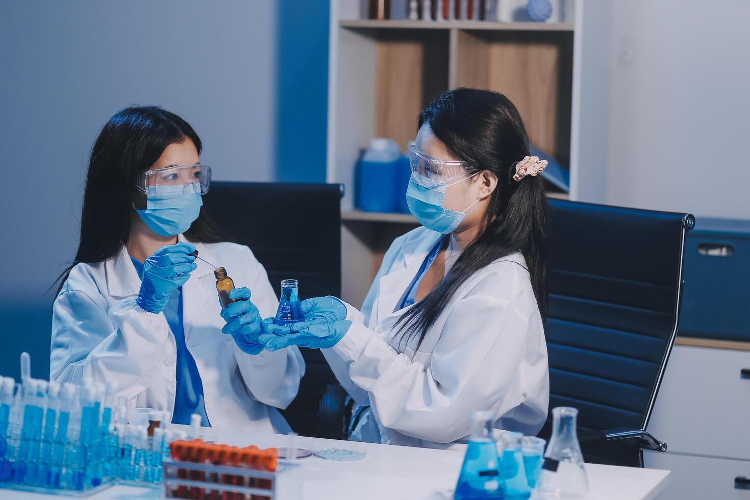 Two women in lab coats and masks holding vials photo