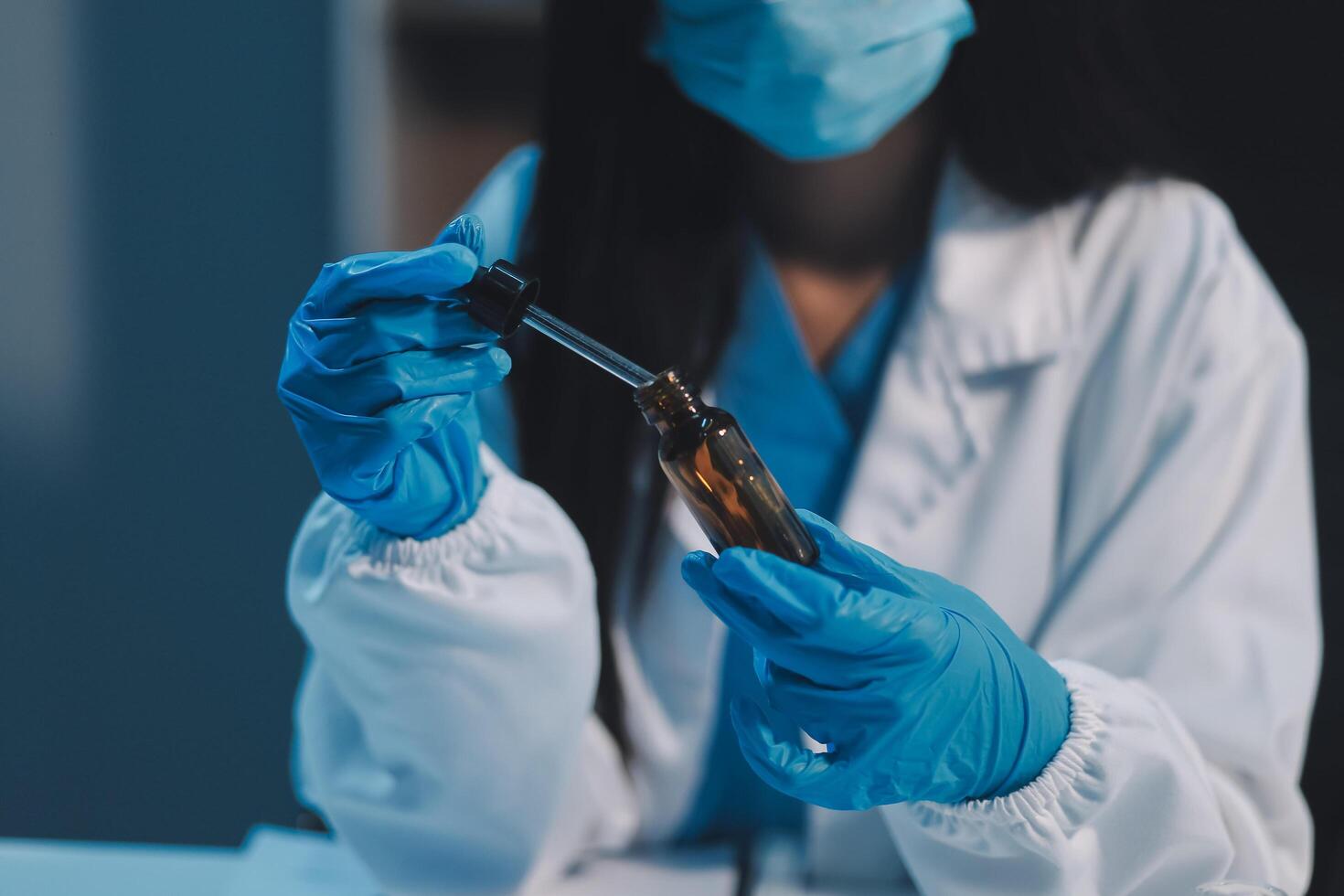 A woman in a lab coat and gloves is holding a glass vial photo