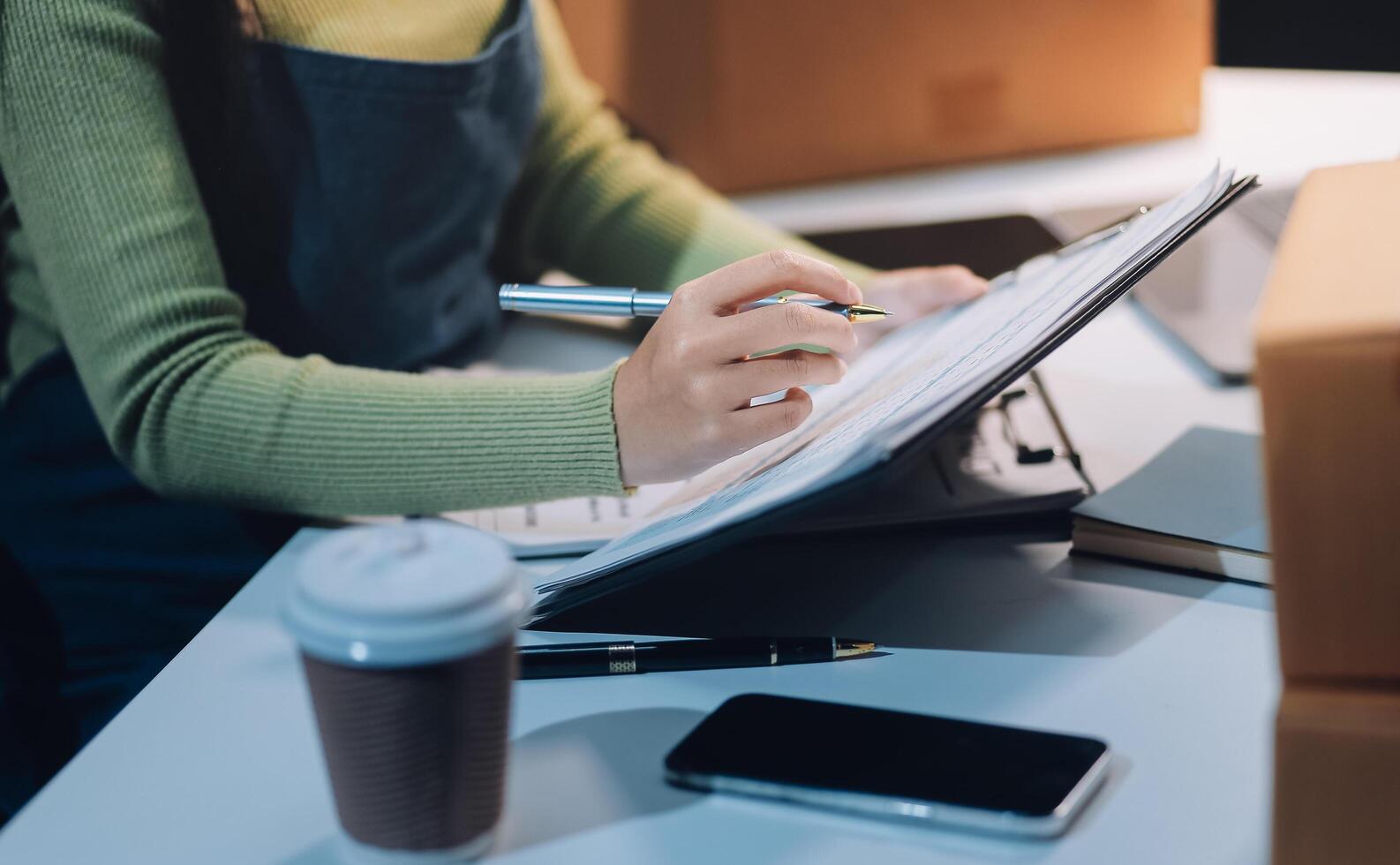 A woman is writing on a clipboard while sitting at a desk with boxes and a cup of coffee photo