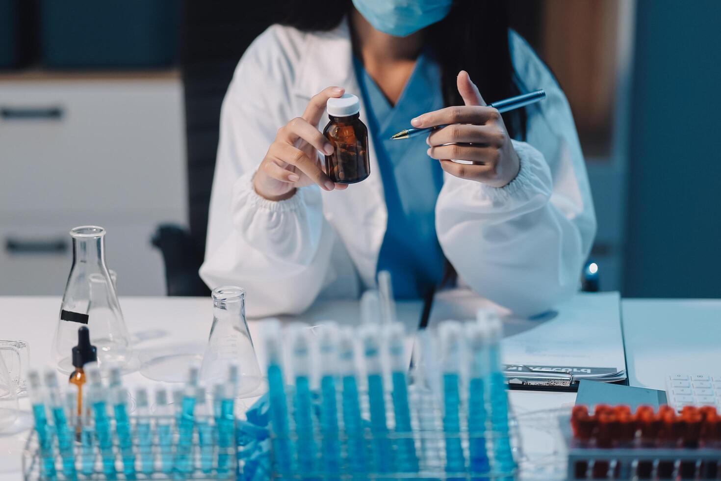 A woman in a lab coat is holding a vial of liquid photo