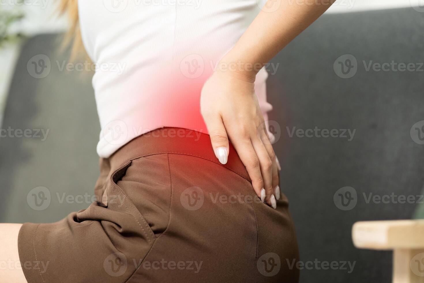Back Pain Relief. Woman experiencing discomfort in lower back while sitting on sofa. photo
