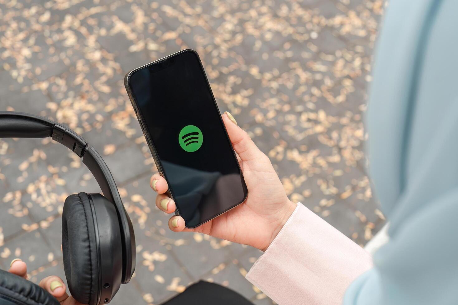 CHIANG MAI ,THAILAND JAN 30 2025 . Apple iPhone 14 Person holding a smartphone with Spotify logo and headphones in autumn. photo