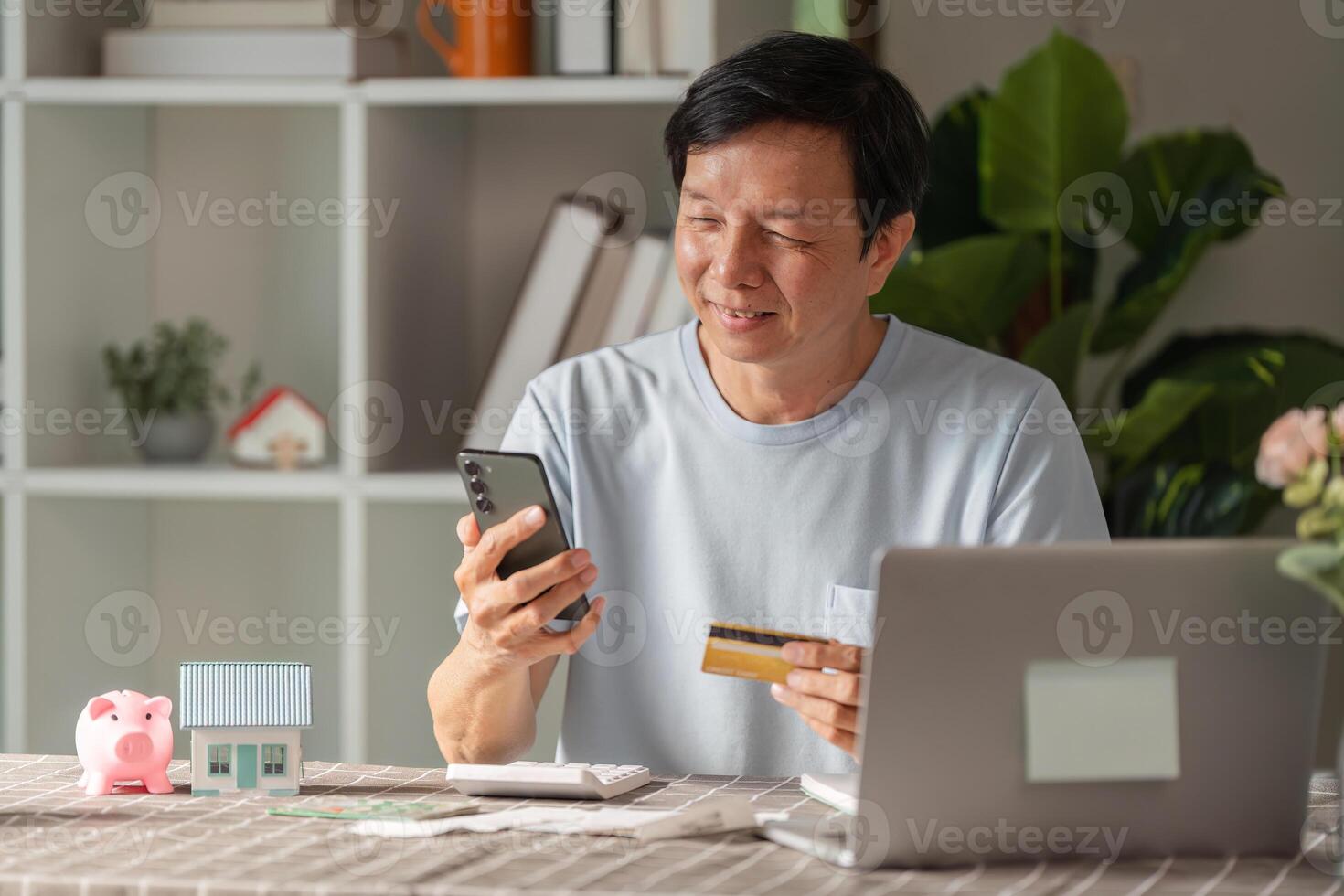 Senior man enjoying online shopping with a credit card and smartphone at home workspace photo