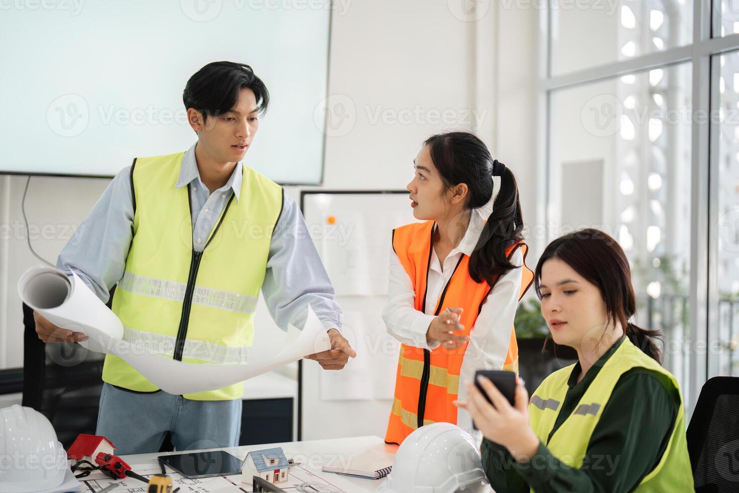 Construction team reviewing blueprints and discussing project details in modern office with safety gear photo