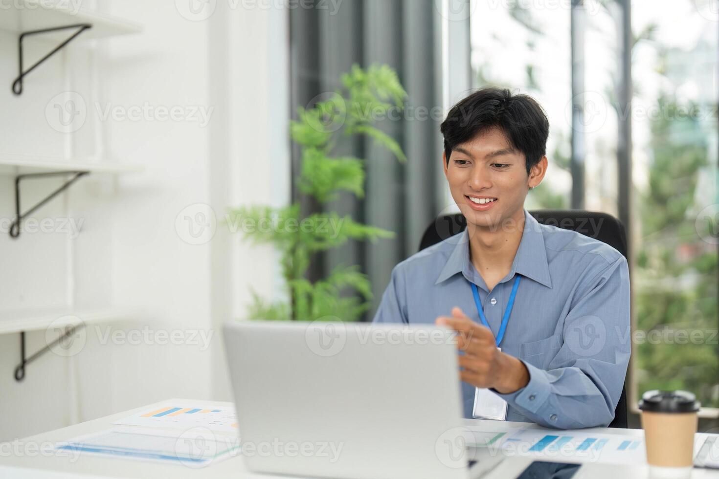 Positive Work Environment. Young man smiling while using laptop in modern office. photo