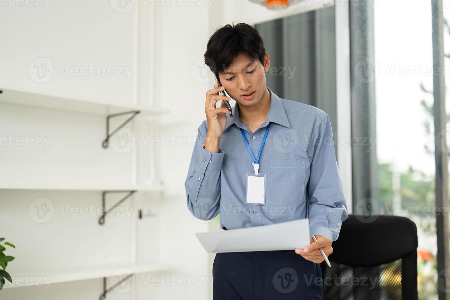 Remote Work and Communication. Young professional reviewing paperwork while on the phone. photo