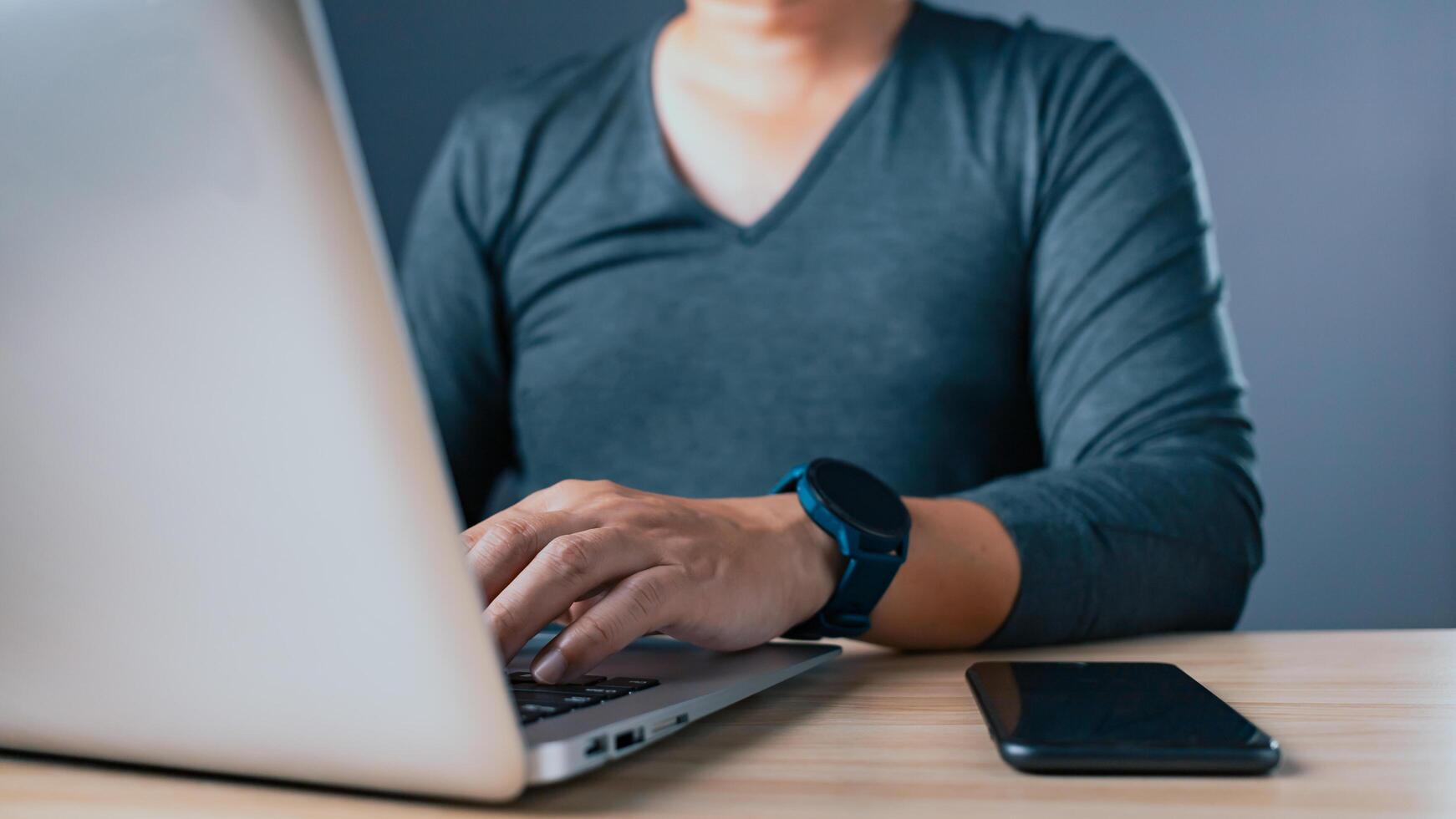 A person types on a laptop while a smartphone rests on a table, symbolizing technology, work, communication, and modern productivity in a professional or home office setting. photo
