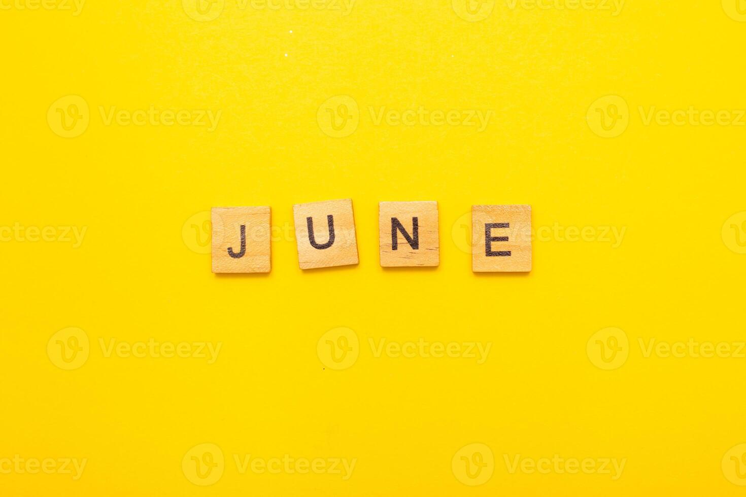 Top view of word June month made by wooden cubes with letters on yellow bright background photo