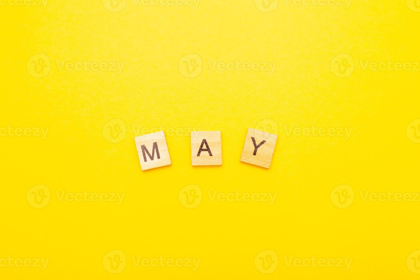 Top view of word May month made by wooden cubes with letters on a yellow bright background photo