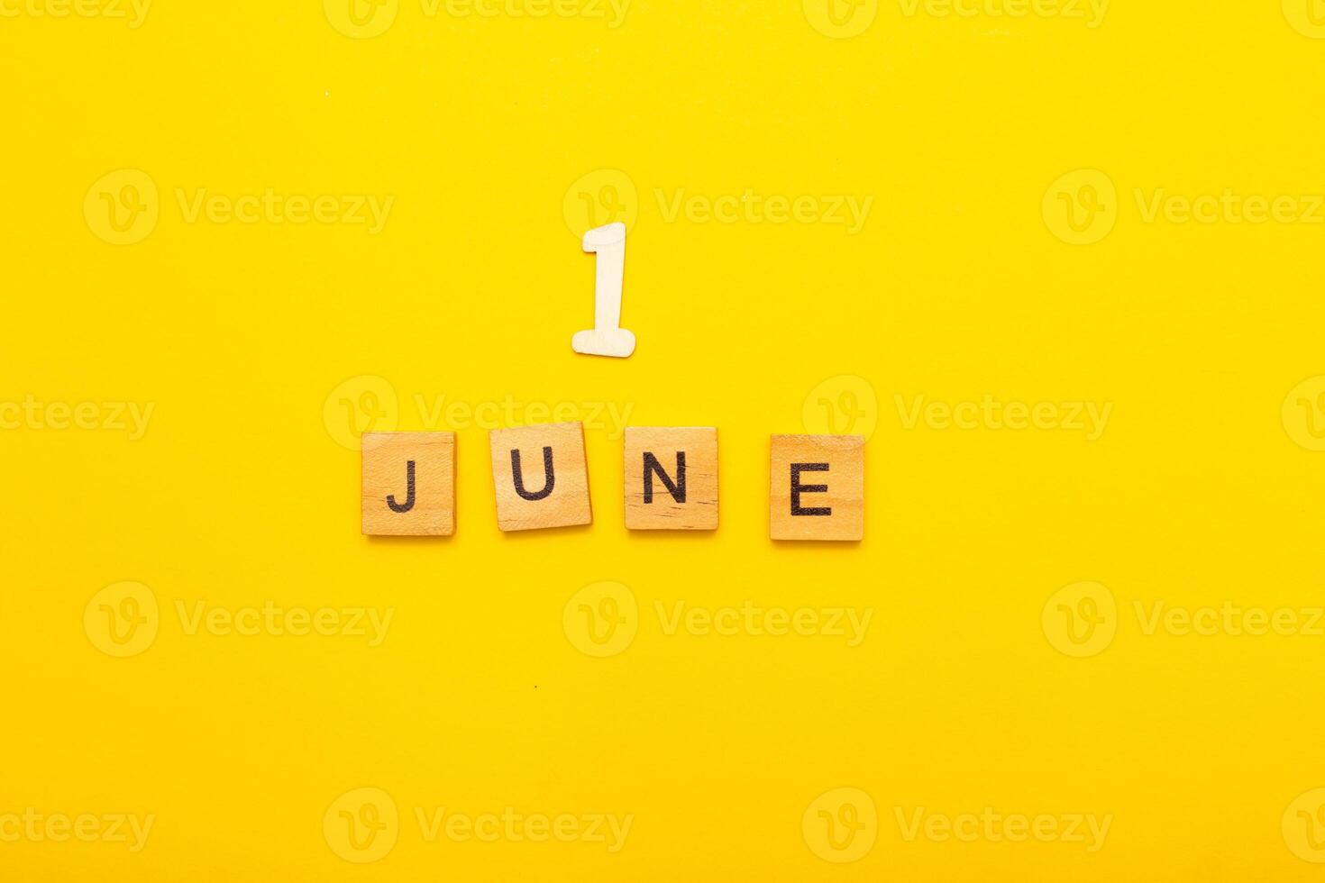 Top view of word June month made by wooden cubes with letters on a yellow bright background. photo