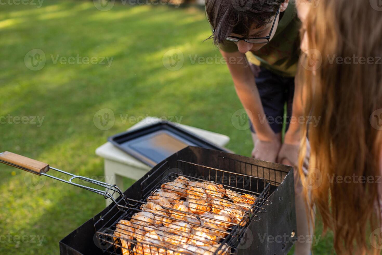 Kida grilling chicken on a barbecue grill in a backyard during summer photo