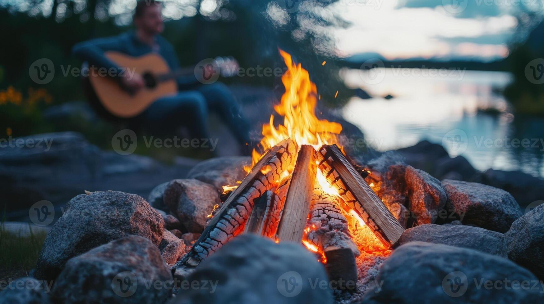 Cozy bonfire surrounded by rocks with a guitarist playing by the lakeside at twilight photo