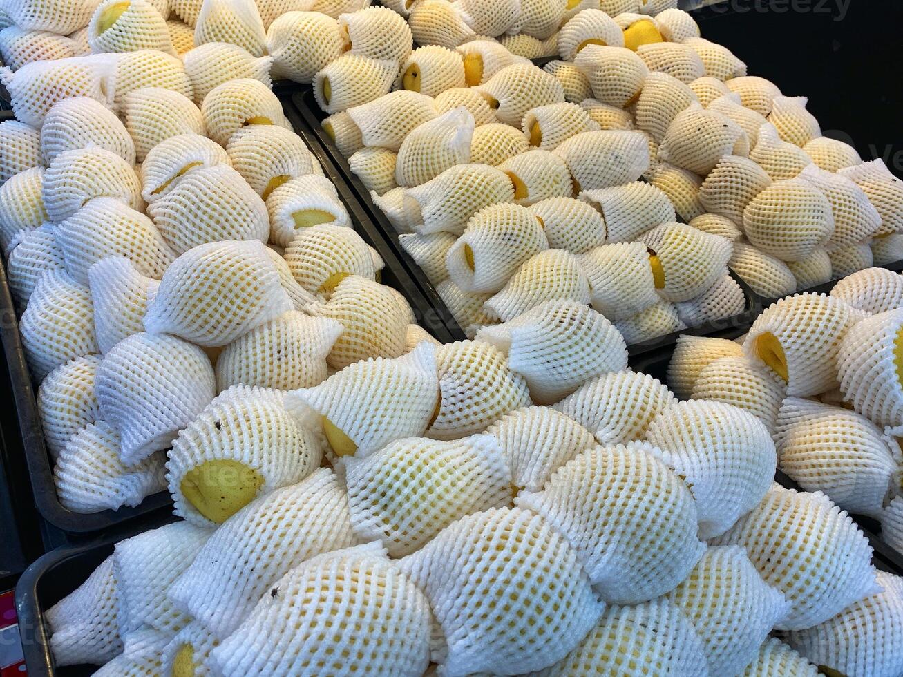 A close-up of neatly arranged yellow pears wrapped in white foam netting, ready for sale at a market or grocery store. photo