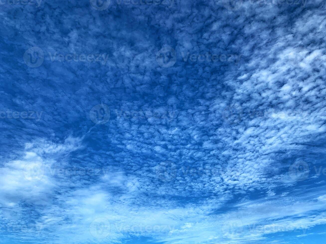 A stunning view of the sky filled with soft, scattered clouds forming intricate patterns across a vivid blue background, evoking peace and wonder. photo