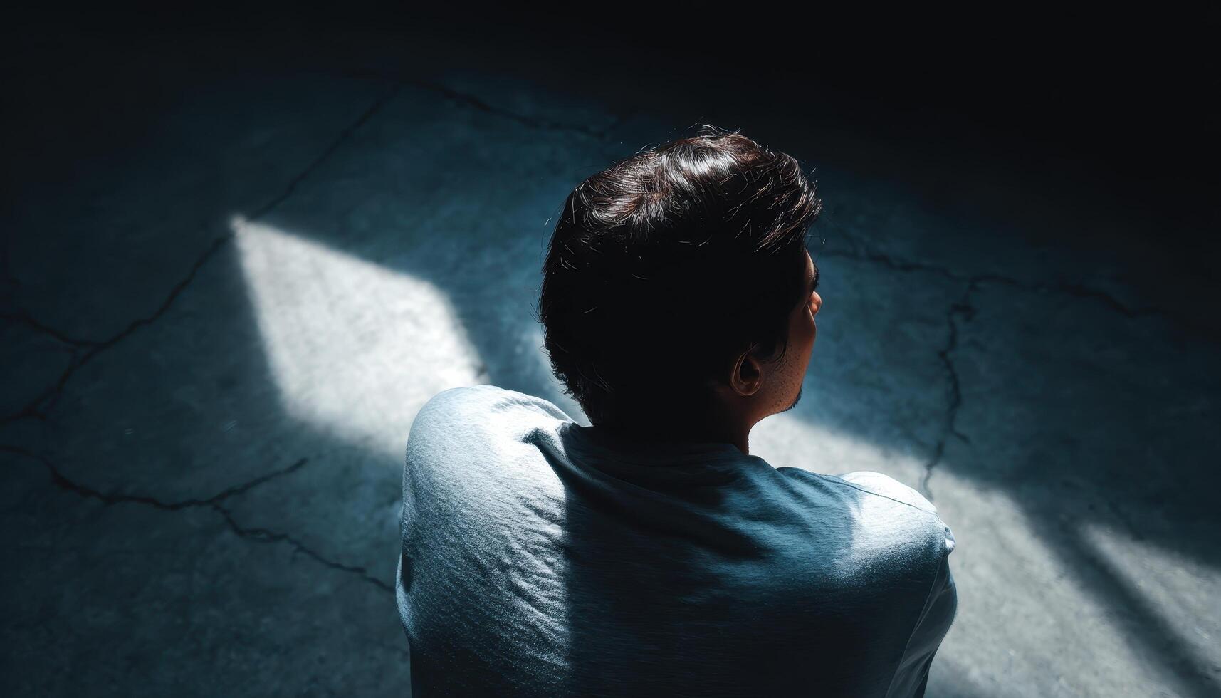 Person contemplating in a dark room with light cracks emotional reflection indoor environment photo