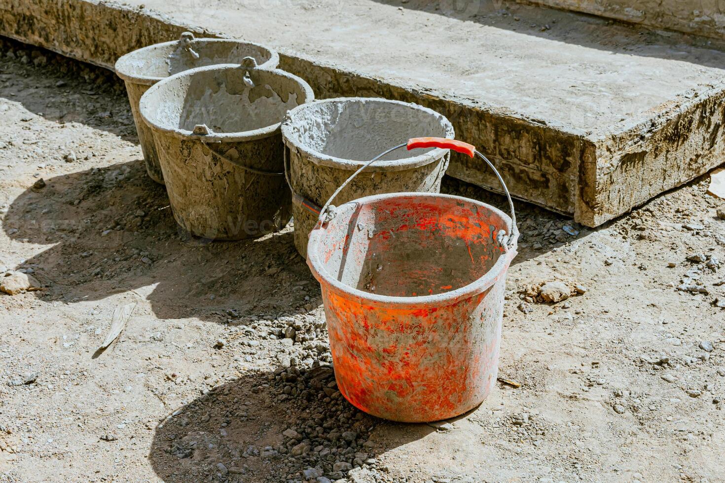 A cement bucket with a red handle sitting on a cement block photo