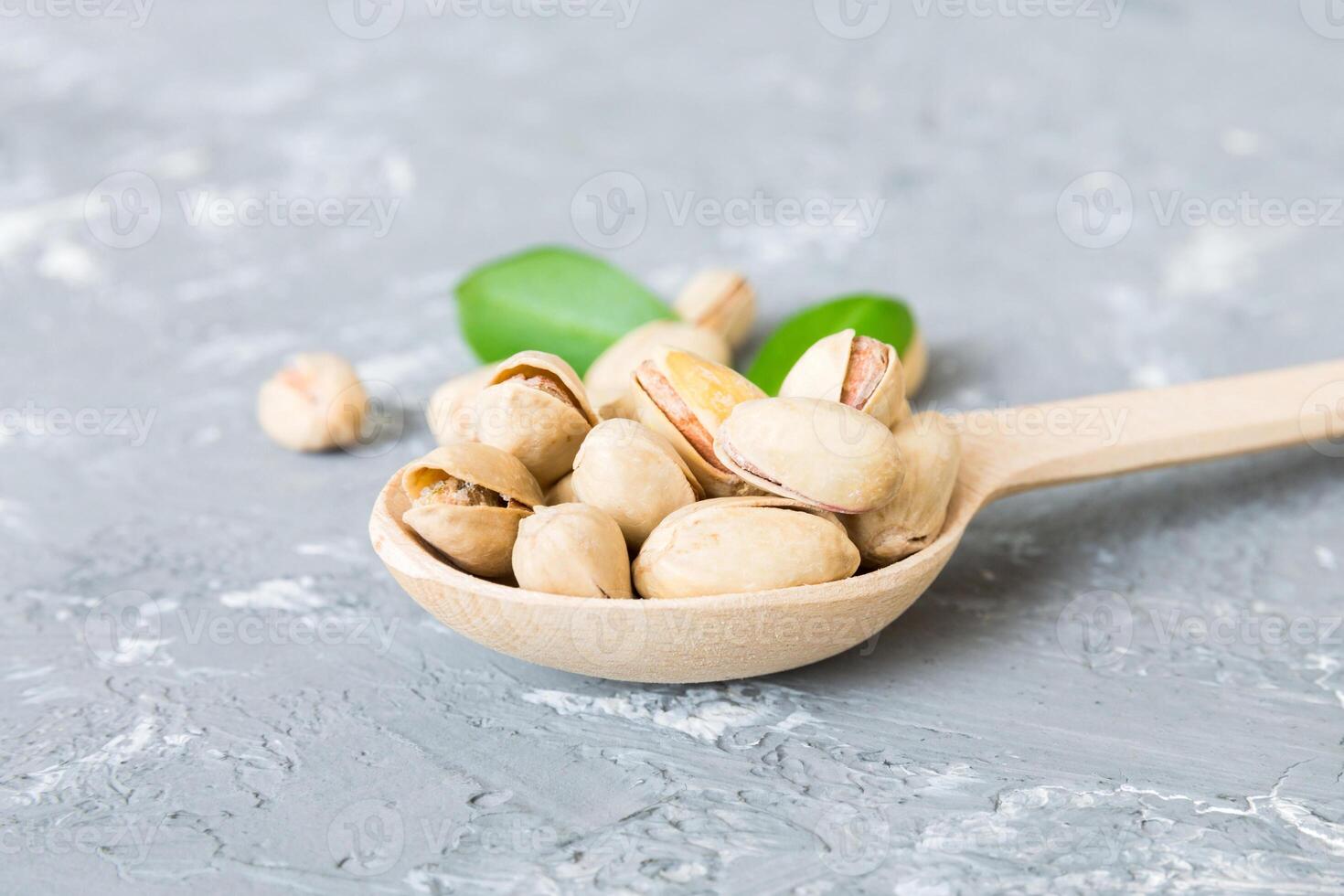 Close-up tasty pistachio nuts in spoon with leaves on table background. Top view. Flat lay photo