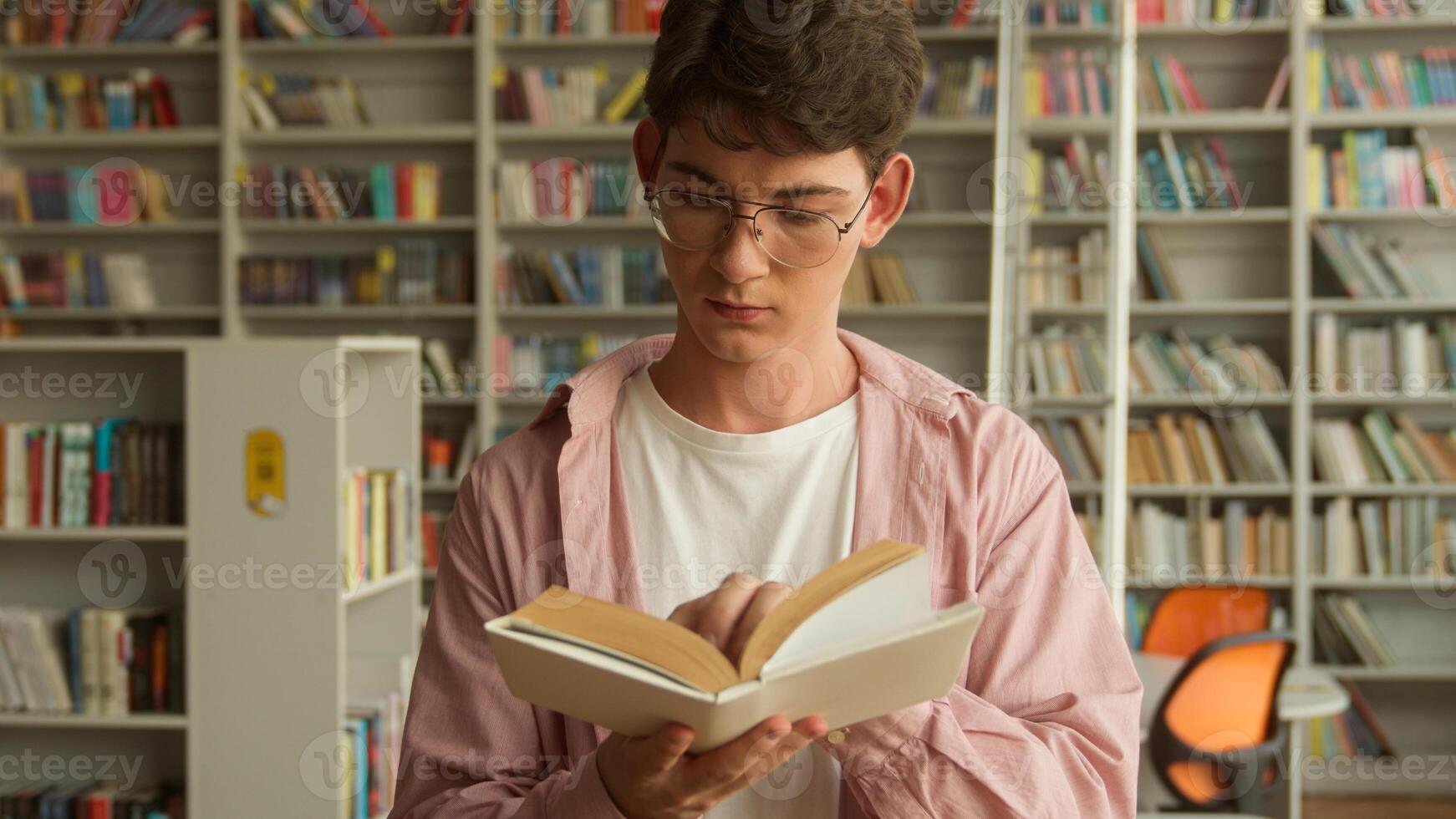 Close up concentrated Caucasian male student man guy teenager reading book poem story textbook turning page in library education studying learning in school college teen study read prepare for exams photo