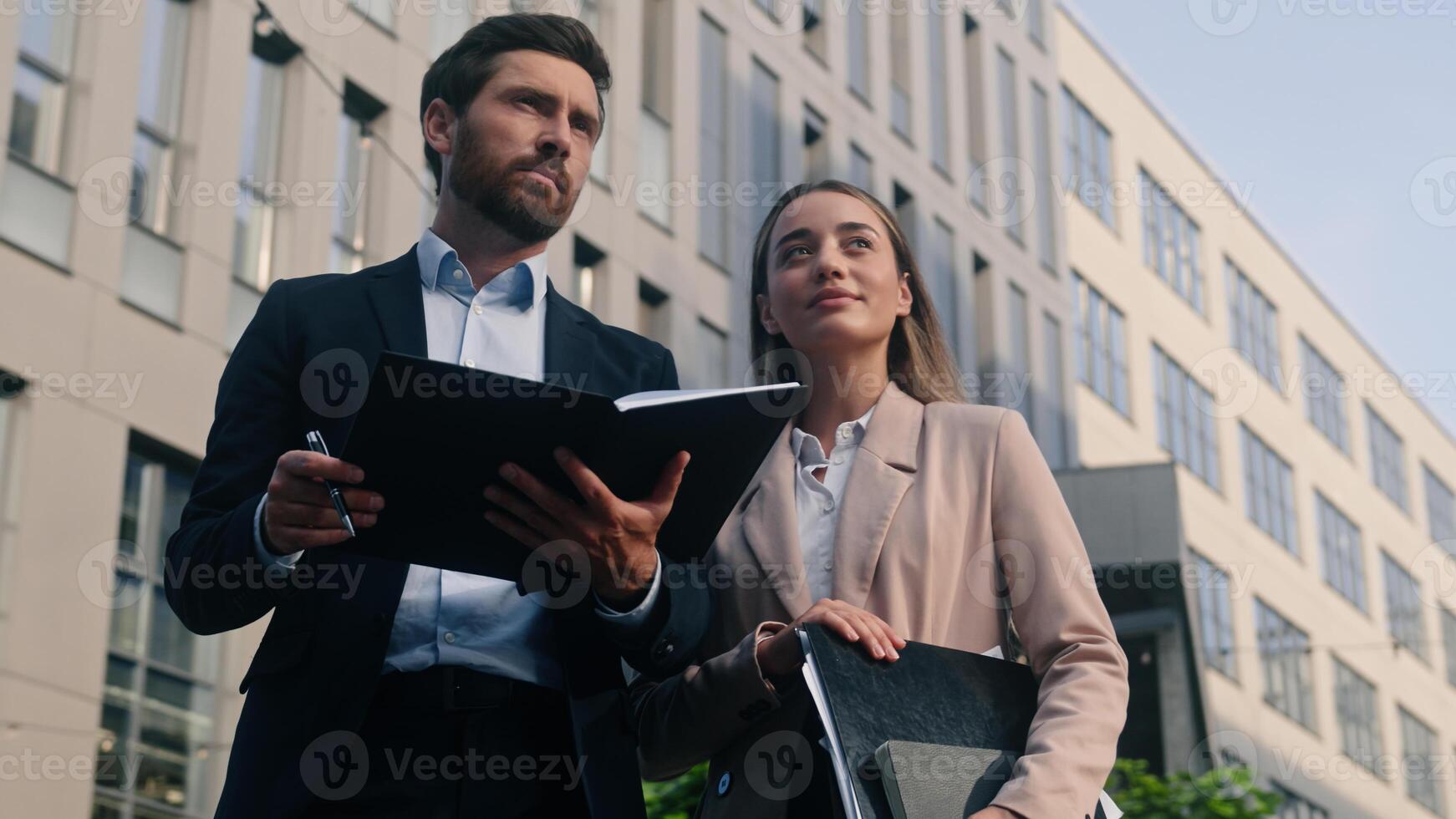 Two business people man and woman communicate in city near office holding folder papers documents male boss talking with female manager discuss work project corporate businessman with businesswoman photo