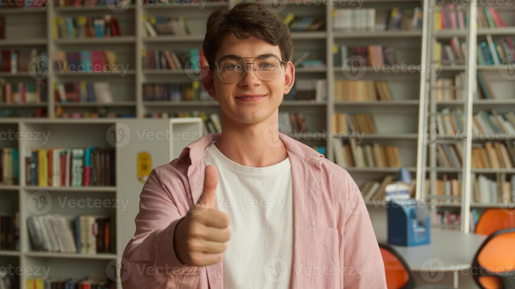 Portrait Caucasian teenager guy showing thumb up like gesture good exams result successful study in school college library teen boy happy smiling recommend education studying learning approve hand photo