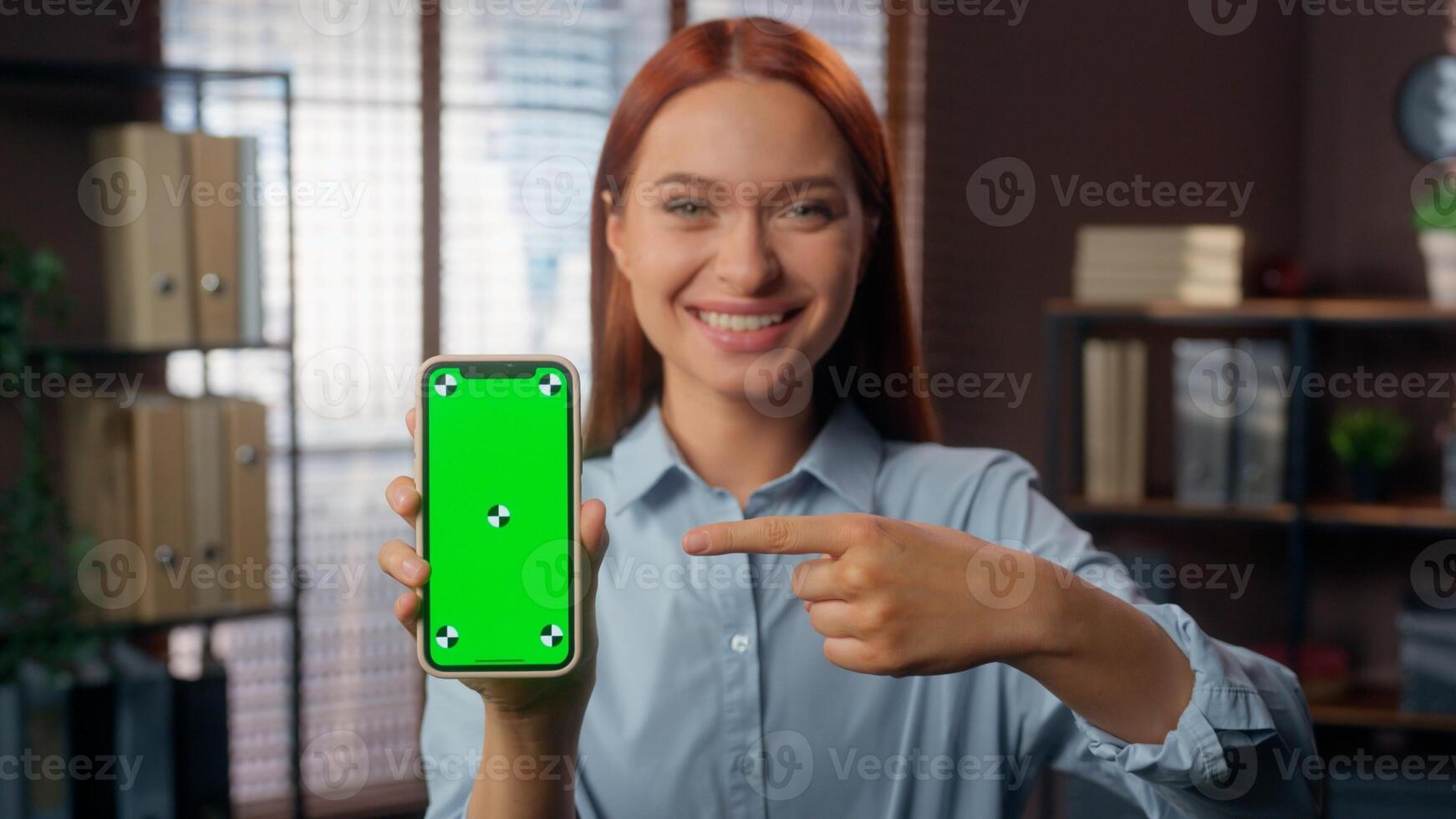 Business woman happy showing green screen mobile phone chroma key pointing with index finger on display businesswoman in office Caucasian female girl employer manager demonstrate online app smartphone photo