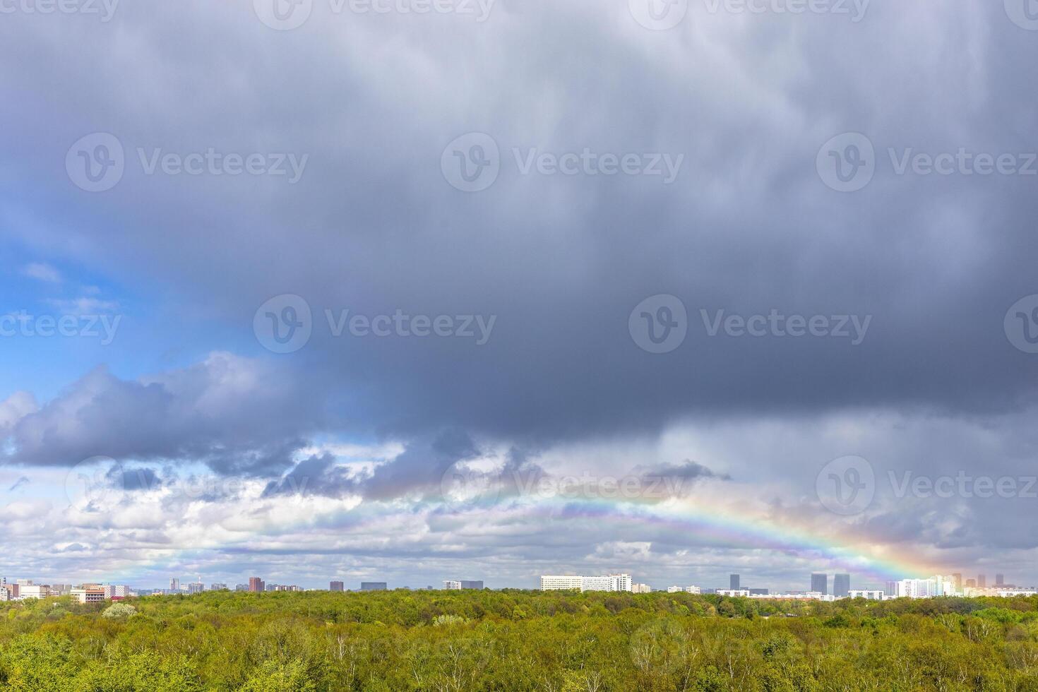 grey rainy clouds and rainbow over green city park photo