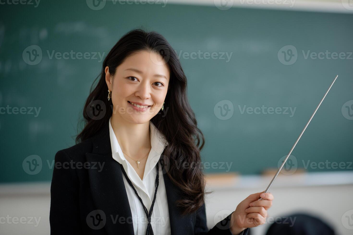Smiling teacher in front of chalkboard, pointing photo