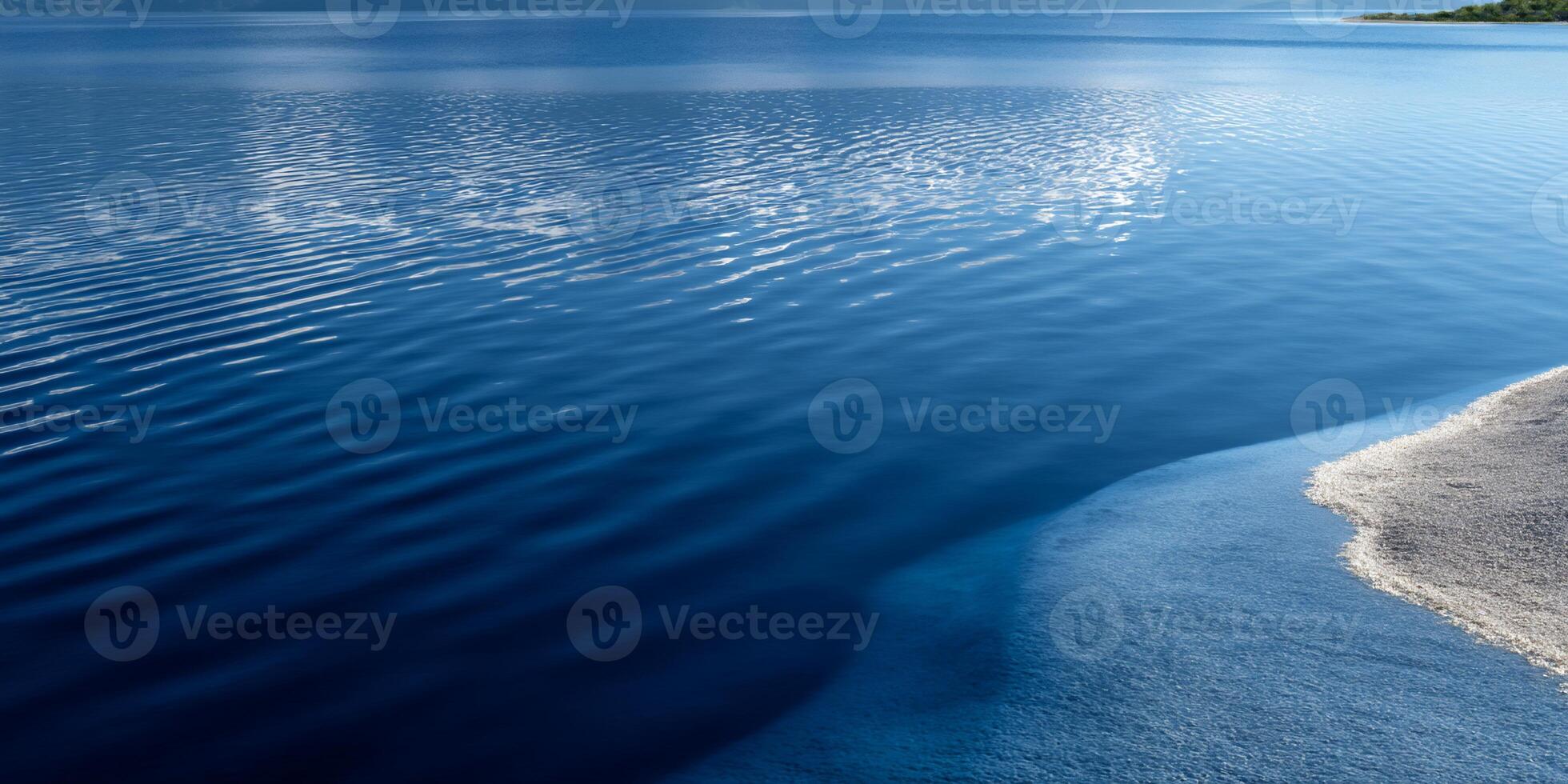 Calm, deep blue water meets a light-colored shoreline photo