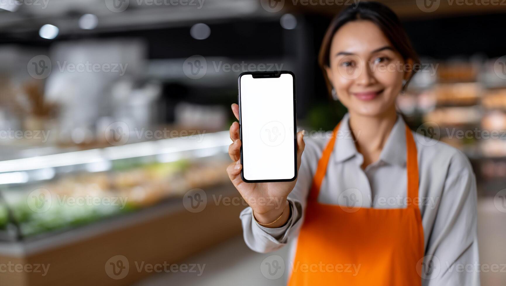 Woman in apron holds phone with blank screen in grocery store photo