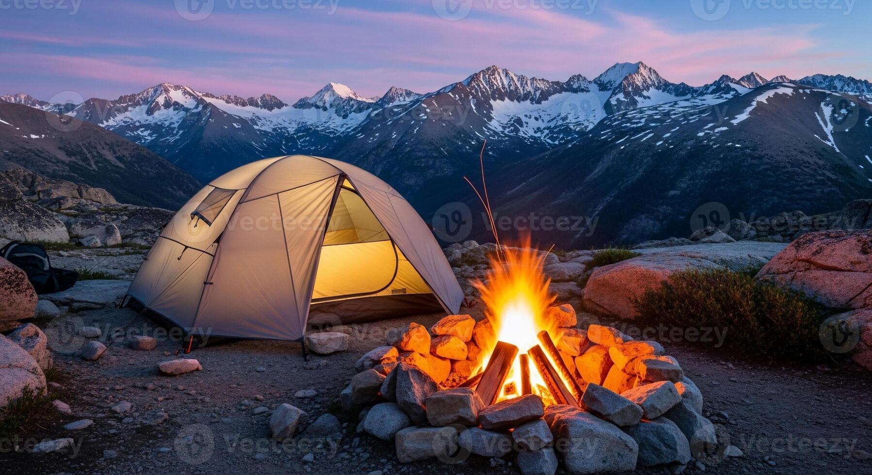 A tent is set up near a campfire in the mountains photo