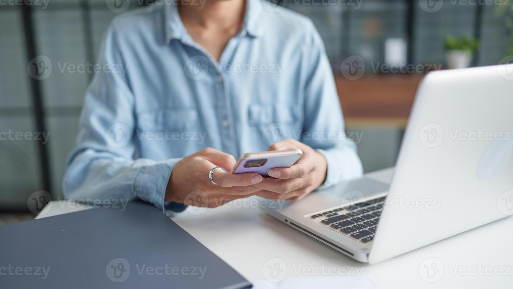 a woman is using her phone while sitting at a desk with a laptop photo