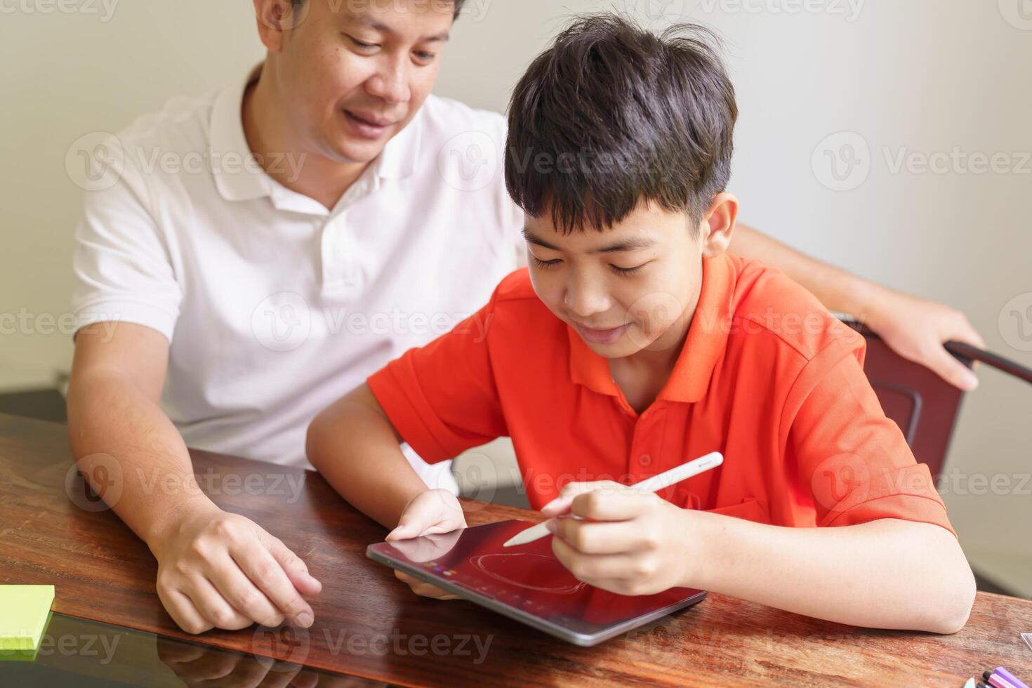 a man and a boy sitting at a table using tablat photo