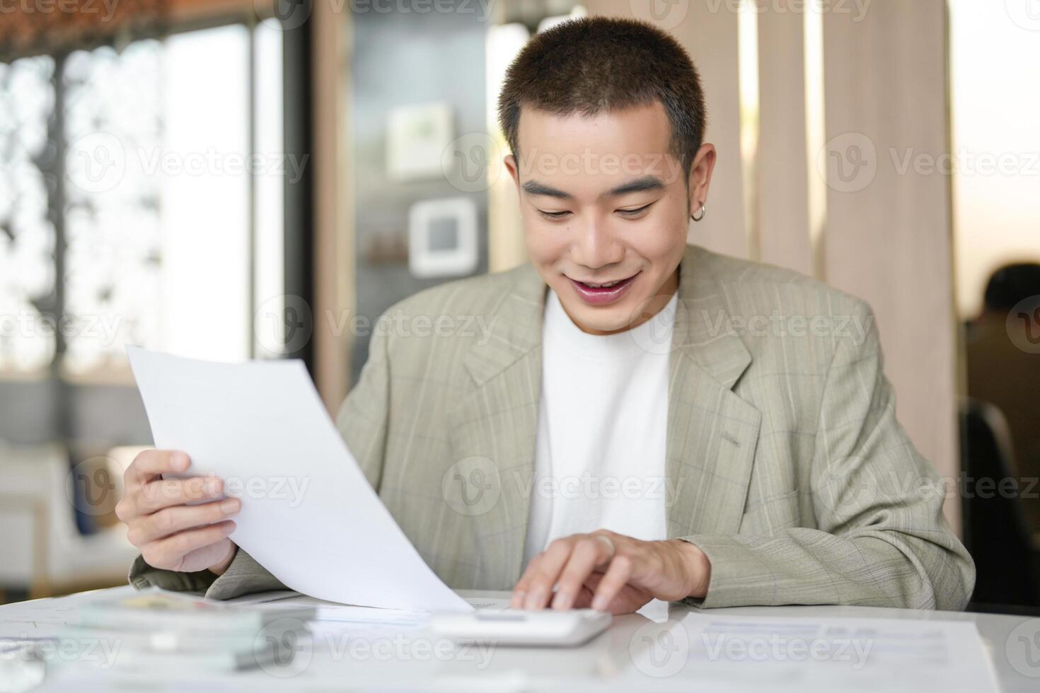 asian man in suit sitting at table with paper and calculator photo