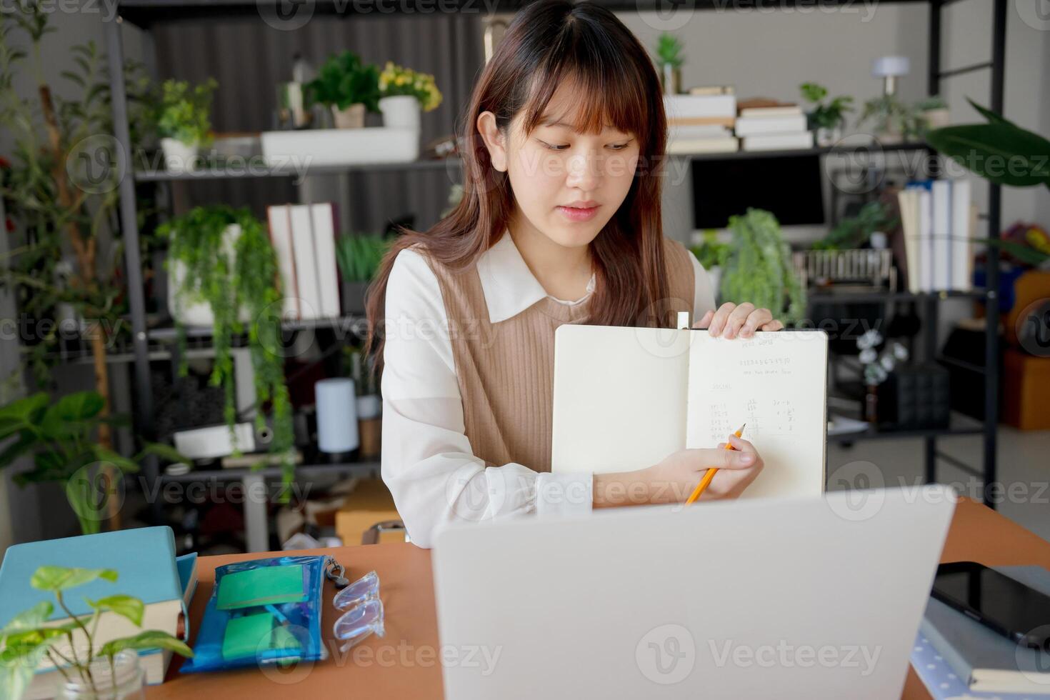 a woman is sitting at a desk with a notebook and a laptop photo