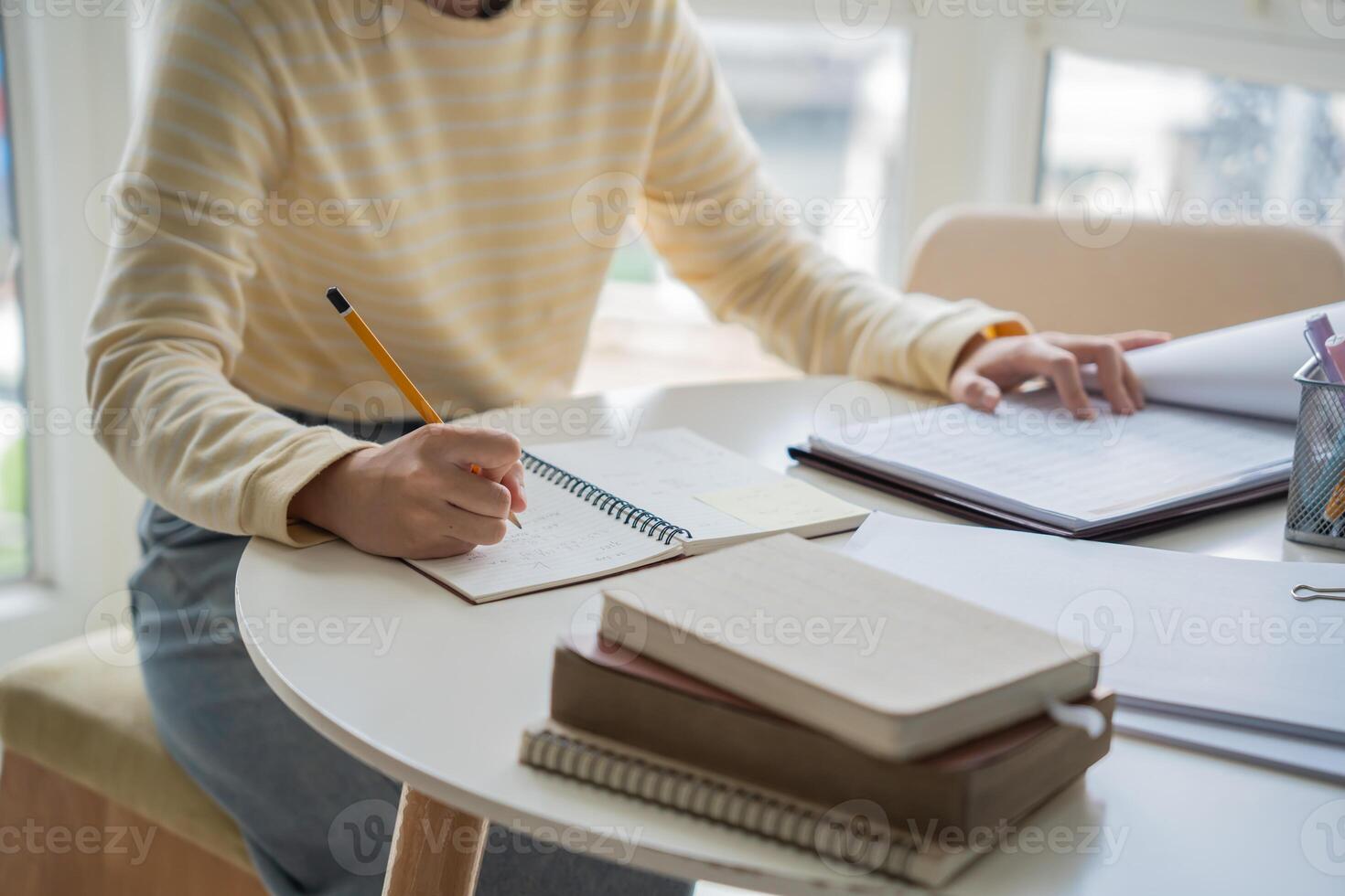 Student asian woman is writing in her notebook at a table with a pen and notebook photo