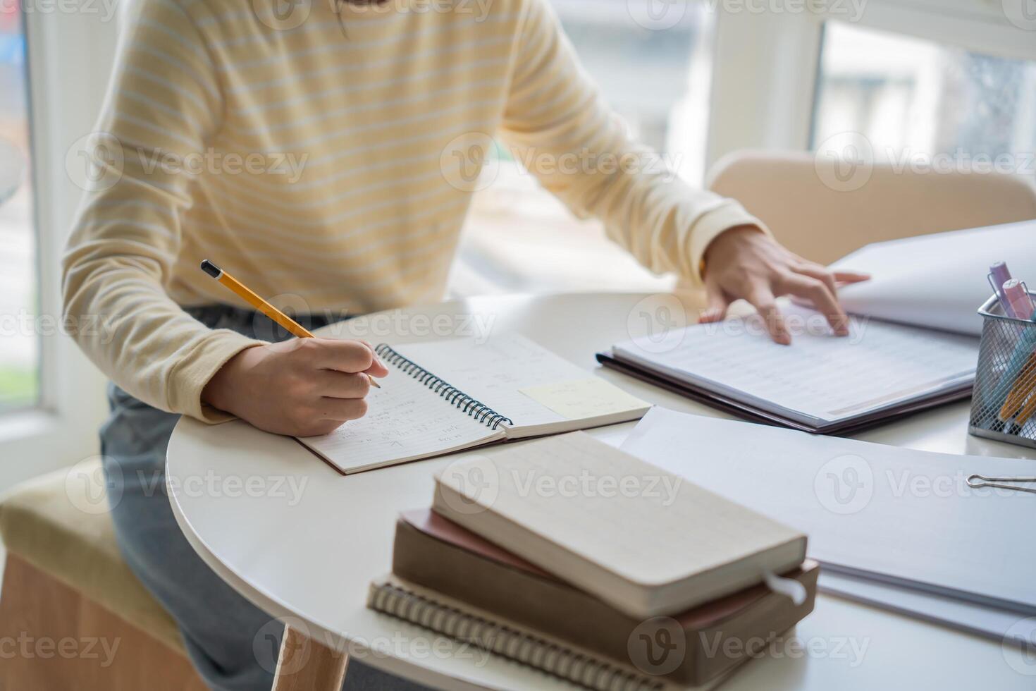 Student woman is writing in her notebook while sitting at a table with a laptop and a notebook photo
