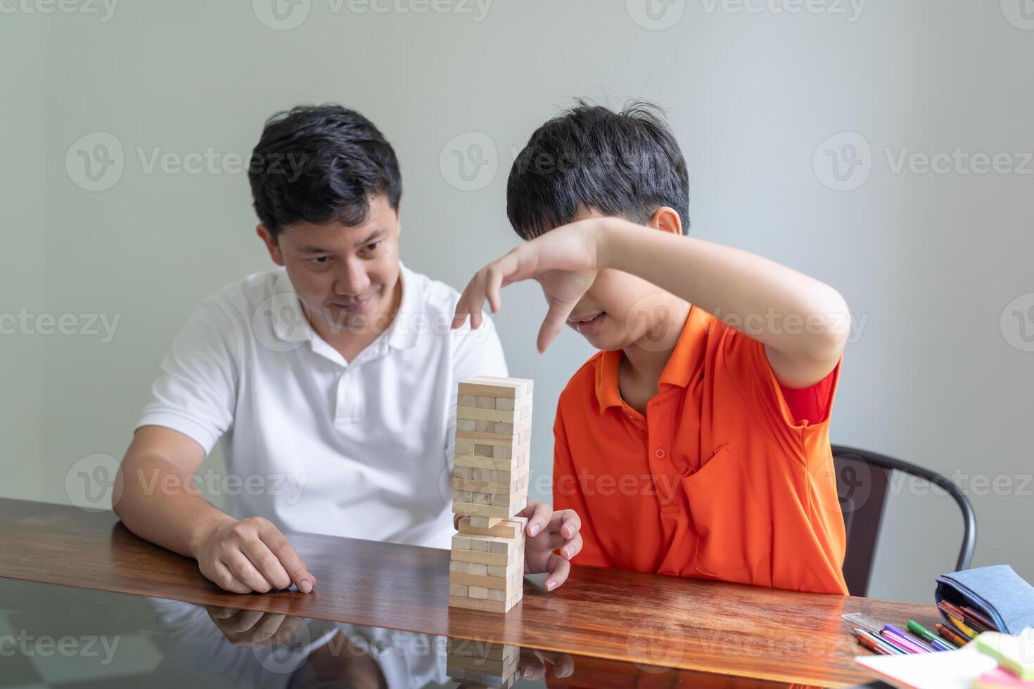 Asian father and son playing wood blocks game Carefree kid playing wood blocks game building constructor from blocks with father at home. photo