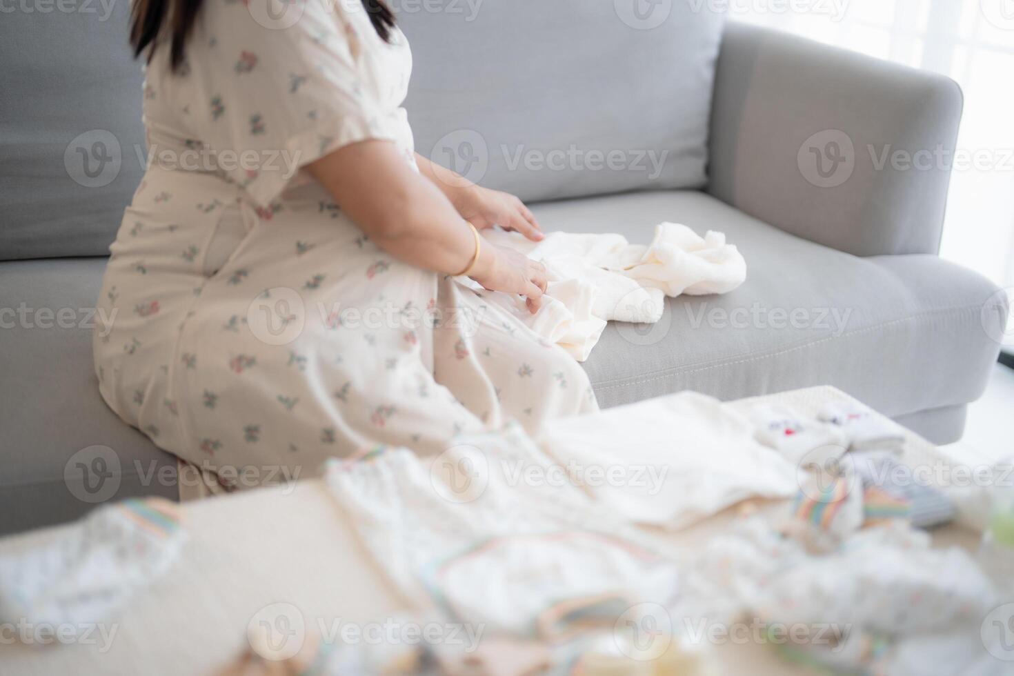 a Pregnant woman sitting on a couch prepare baby clothes. photo