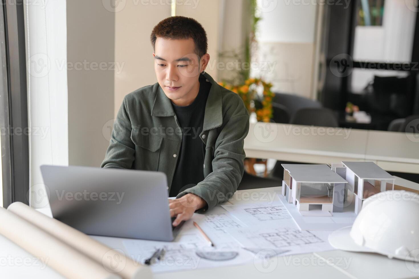 a man in a green jacket sitting at a table with a laptop. photo