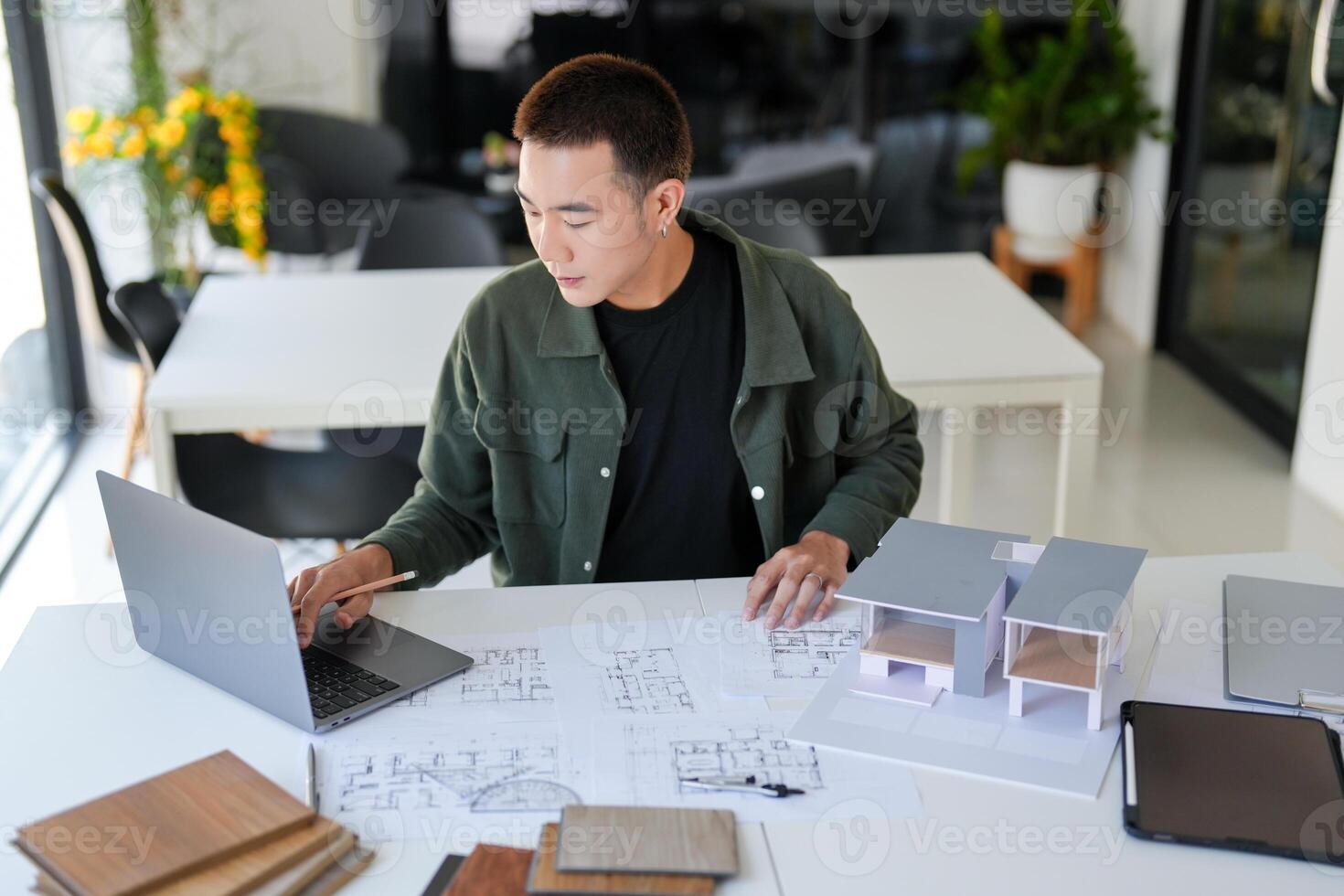 a man working on a laptop in front of a desk with architectural plans photo