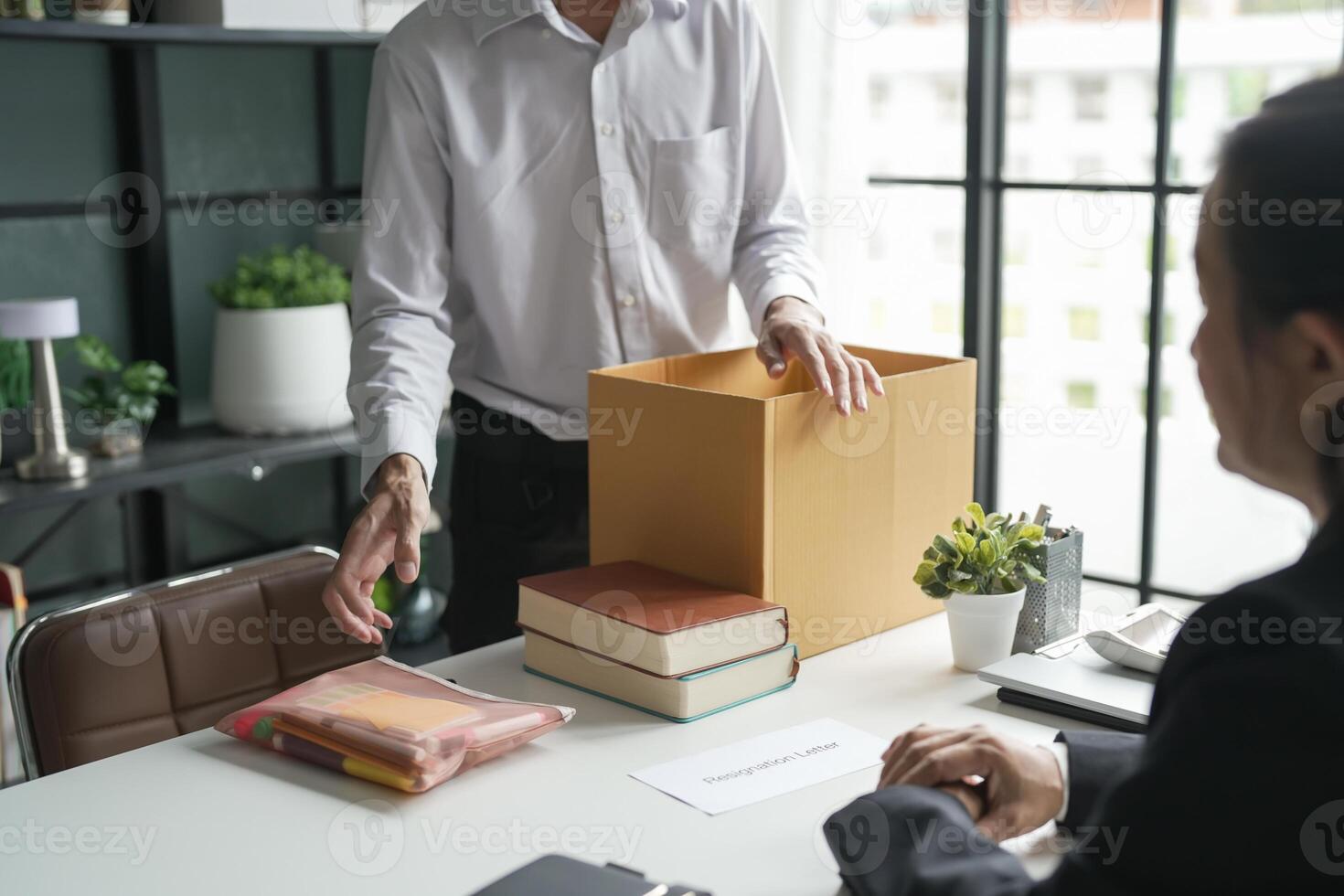 a man is opening a box with papers and a woman is sitting at a desk photo