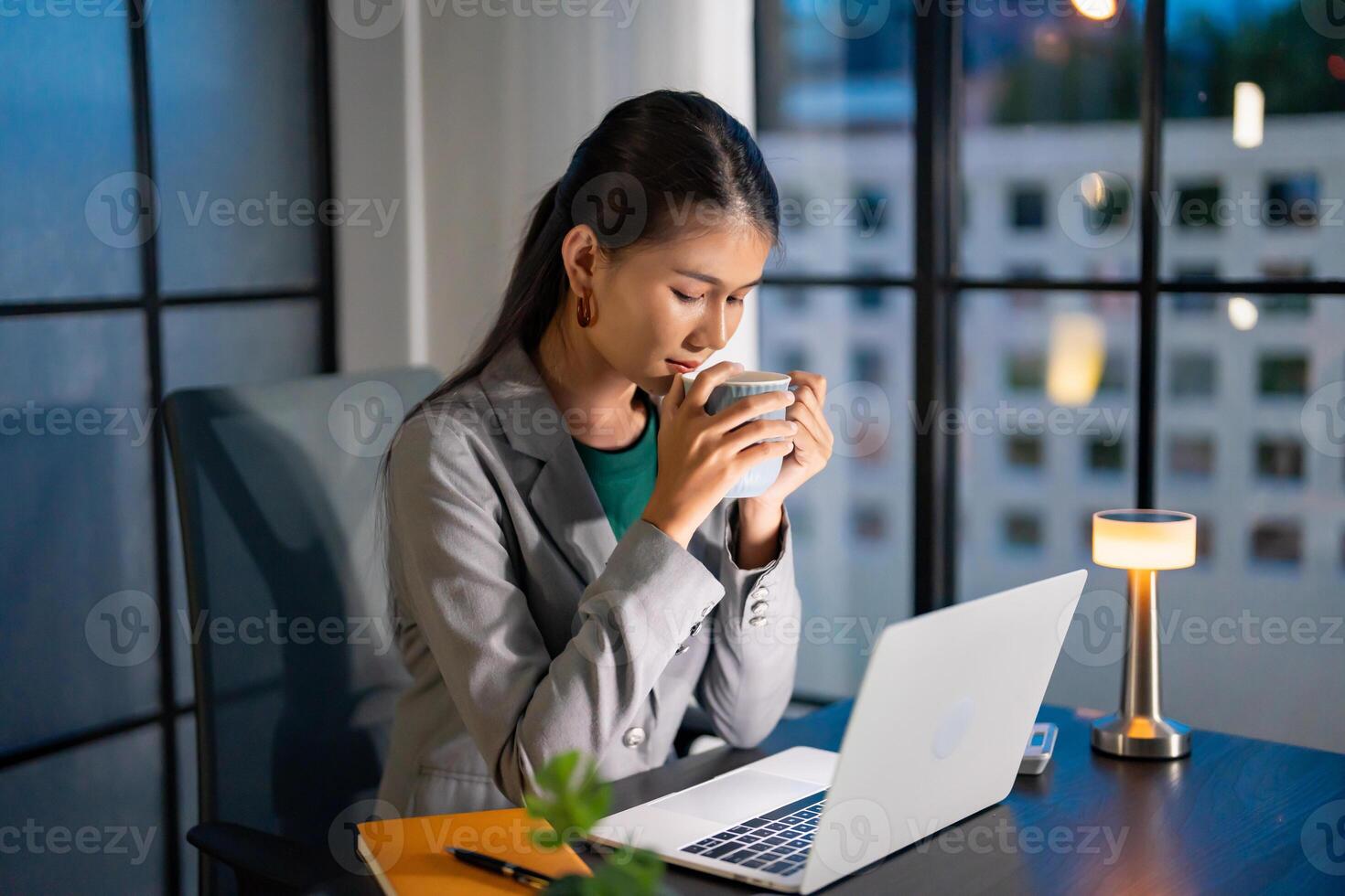 a woman in a business suit sitting at a desk with a laptop. photo