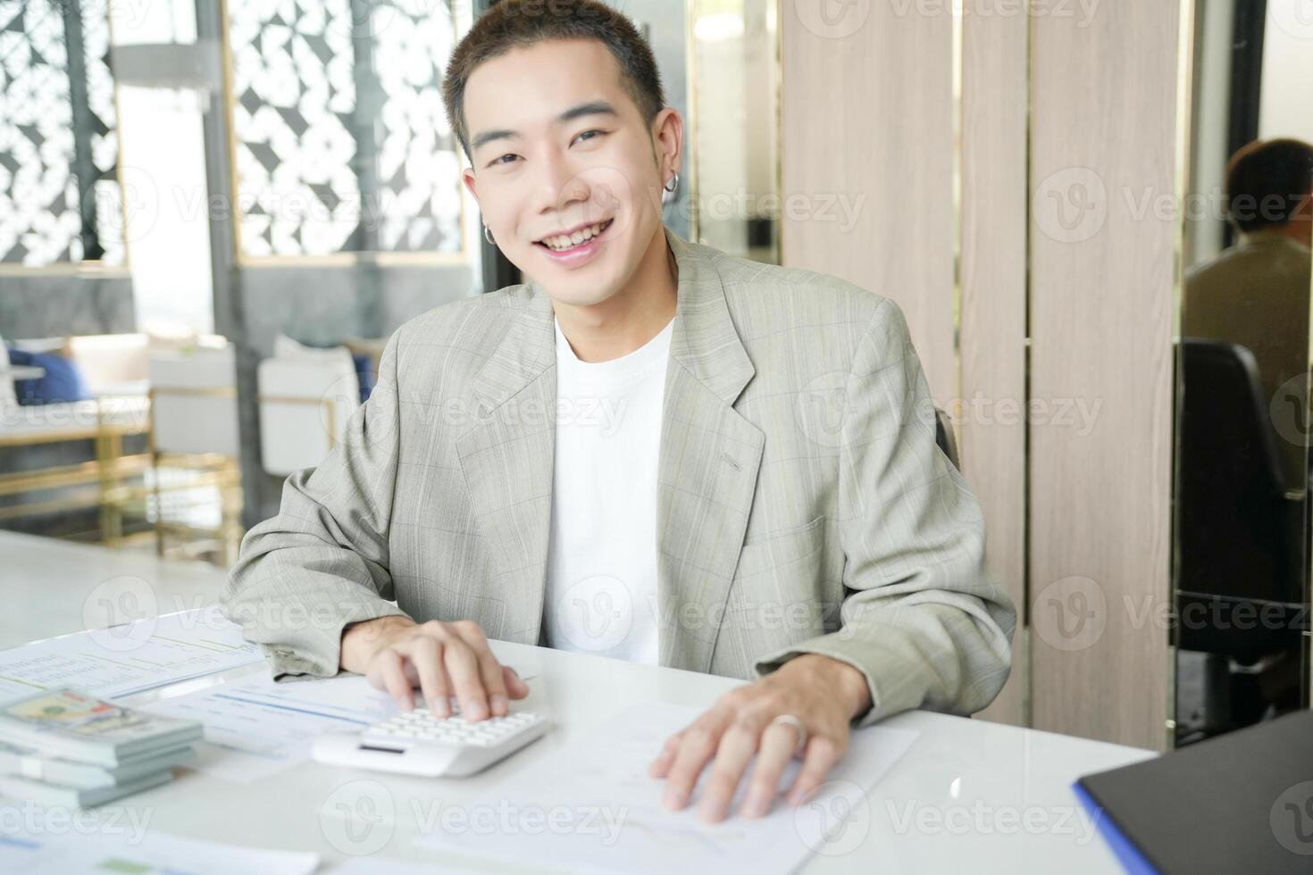 asian man in suit sitting at desk with calculator photo