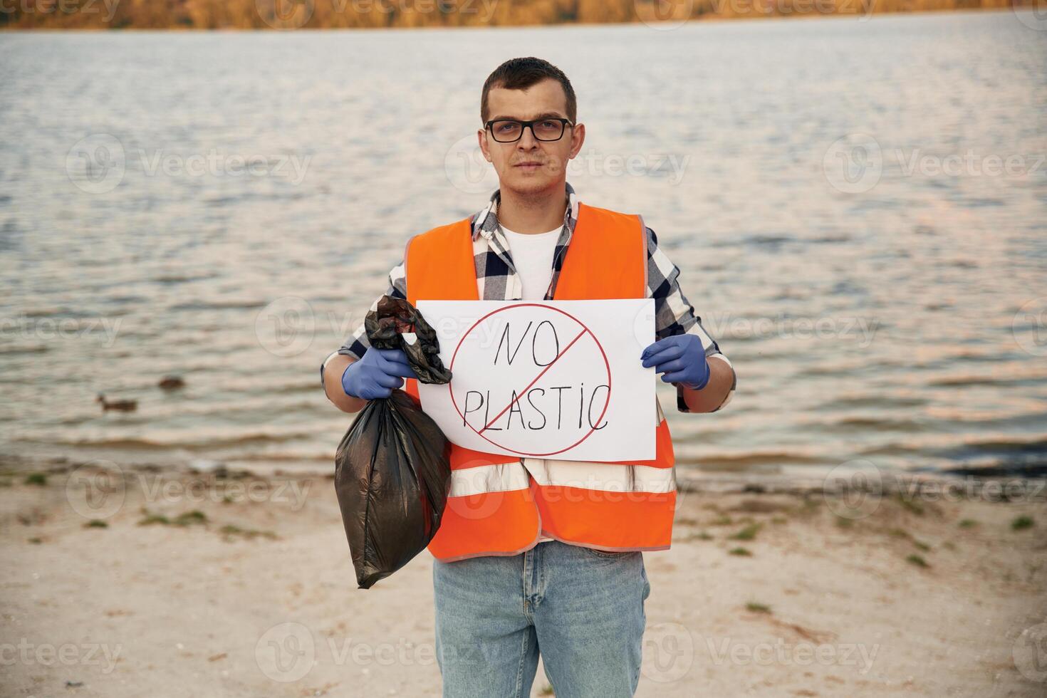 Text, 'no plastic' on poster. Man volunteer is against Earth pollution by trash, outdoors photo