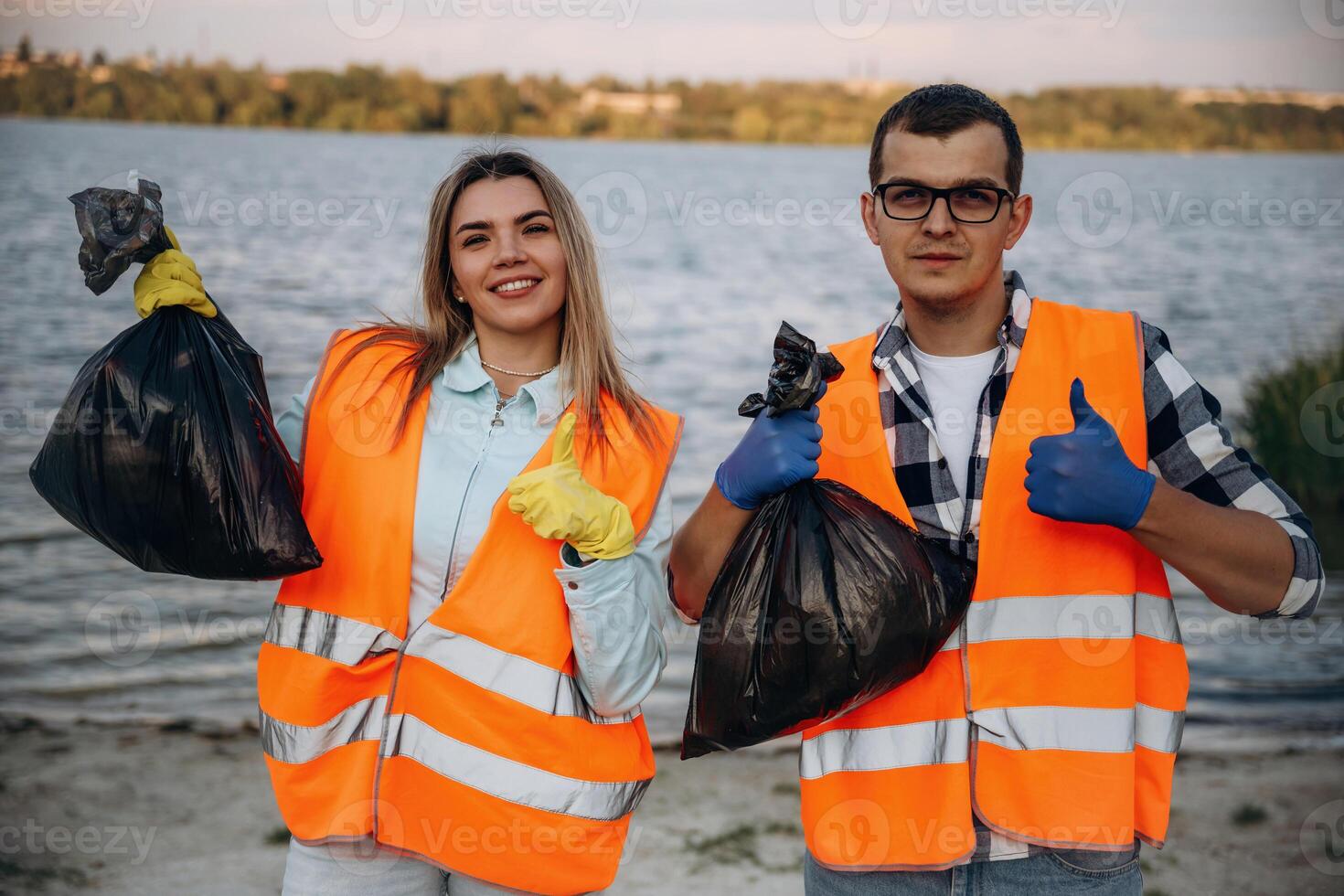 Showing ,fingers, up, smiling, finished. A volunteers collects garbage on a muddy beach photo