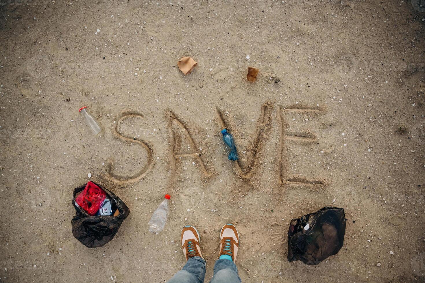 Top view, of sand with word save, trash on the ground, legs of the person, conception of ecology photo