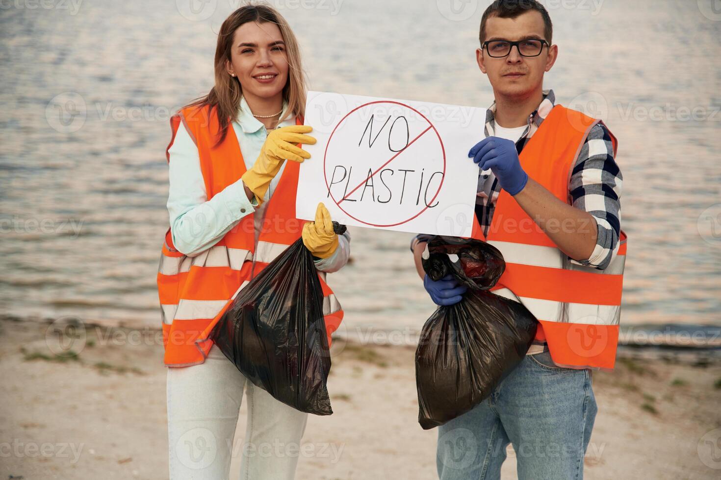 Poster ,with 'no plastic' text. A volunteers collects garbage on a muddy beach photo
