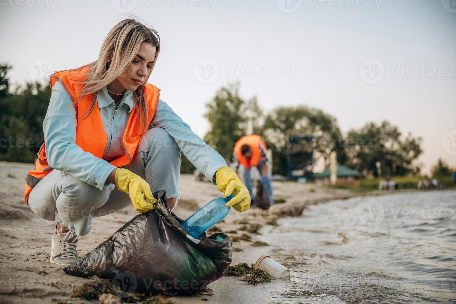 On the shore... A volunteers collects garbage on a muddy beach photo