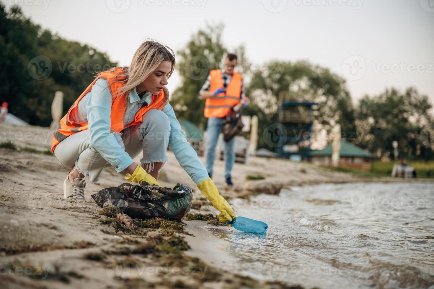 Picking ,bottle, from the water. A volunteers collects garbage on a muddy beach photo
