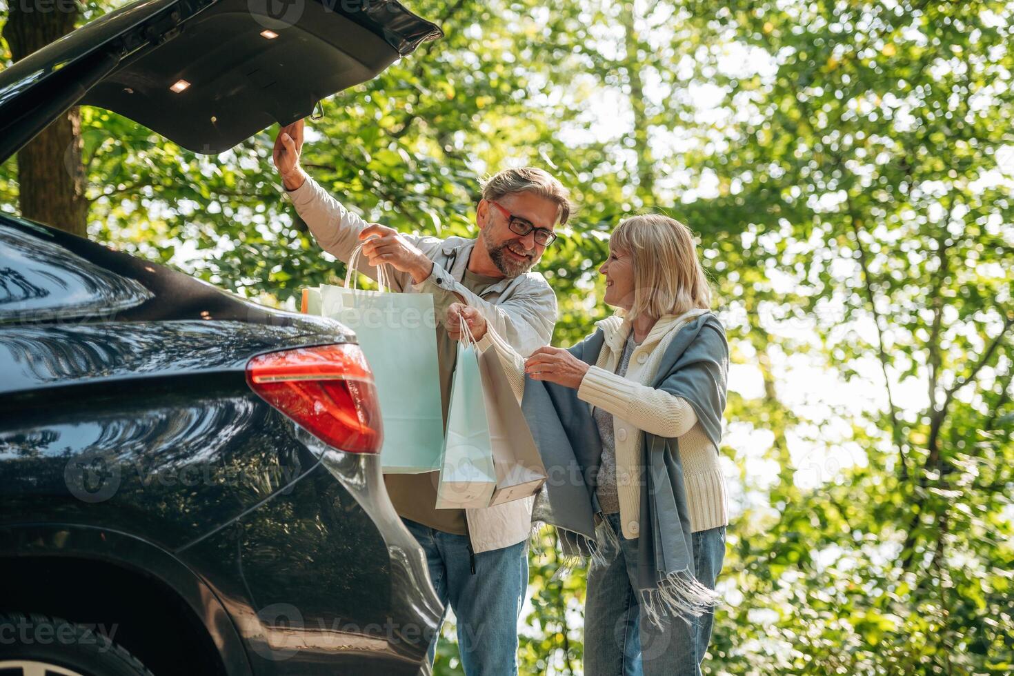 Trunk, is opened,,, holding, shopping bags. Senior couple together outdoors at nature photo